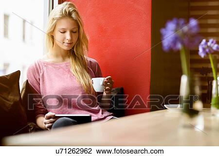 Young woman in cafe window seat drinking coffee and using digital tablet View Large Photo Image Stock Image - Young woman in cafe window seat drinking coffee and using digital tablet. Fotosearch