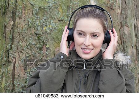 Young woman in front of park tree listening to headphone music View Large Photo Image Stock Image - Young woman in front of park tree listening to headphone music. Fotosearch