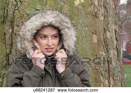 Young woman in front of park tree wrapping up in fur hood View Large Photo Image Stock Photo - Young woman in front of park tree wrapping up in fur hood. Fotosearch