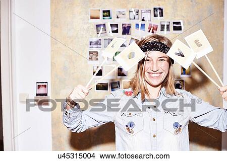 Young woman in front of photo wall holding up love sign View Large Photo Image Picture - Young woman in front of photo wall holding up love sign. Fotosearch
