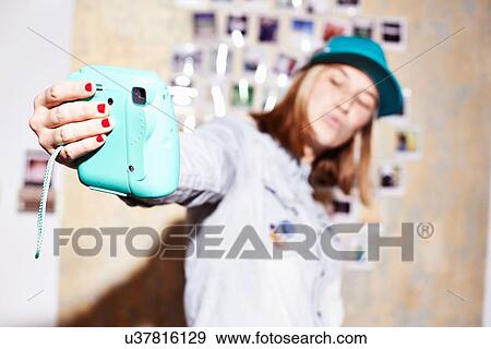 Stock Photo - Young woman in front of photo wall posing for instant selfie. Fotosearch