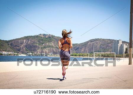 Stock Image - "Young woman jogging on beach, Rio de Janeiro, Brazil". Fotosearch