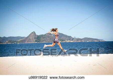 Stock Image - "Young woman jumping on beach, Rio de Janeiro, Brazil". Fotosearch