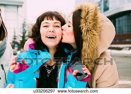 Stock Photo - Young woman kissing friend on cheek. Fotosearch
