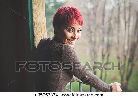 Picture - "Young woman leaning against balcony railings, smiling". Fotosearch