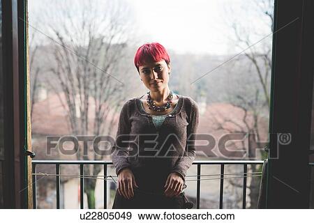 Stock Photo - "Young woman leaning against balcony railings, smiling". Fotosearch