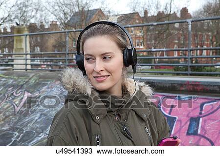 Stock Image - Young woman listening to headphone music in skatepark. Fotosearch