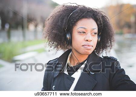 Stock Image - "Young woman listening to headphones in park at Lake Como, Italy". Fotosearch