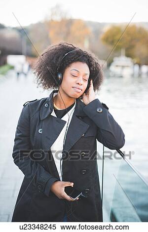 Stock Photography - "Young woman listening to headphones with eyes closed at Lake Como, Italy". Fotosearch