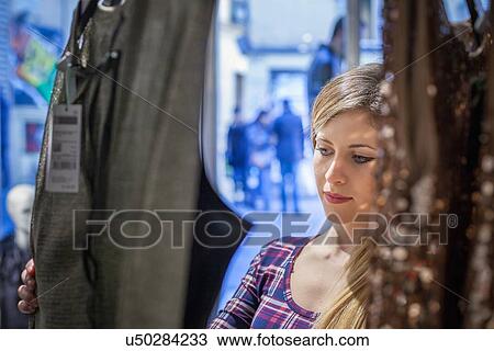 Stock Image - Young woman looking at dresses in boutique. Fotosearch