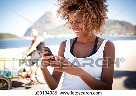 Stock Photography - "Young woman looking at smartphone, smiling". Fotosearch