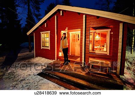 Stock Photo - "Young woman looking out from cabin porch at night, Posio, Lapland, Finland". Fotosearch