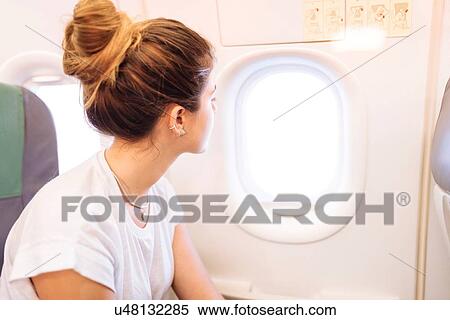 Stock Photography - Young woman looking out of airplane window. Fotosearch