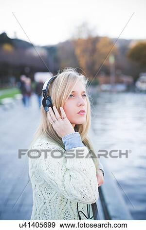 "Young woman looking up whilst listening to headphones on lakeside, Como, Italy" View Large Photo Image Stock Photo - "Young woman looking up whilst listening to headphones on lakeside, Como, Italy". Fotosearch