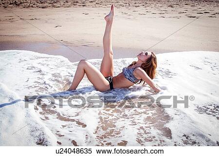 Stock Photography - Young woman lying in ocean with leg raised. Fotosearch