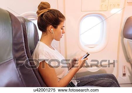 Young woman on airplane choosing music on smartphone View Large Photo Image Stock Photography - Young woman on airplane choosing music on smartphone. Fotosearch