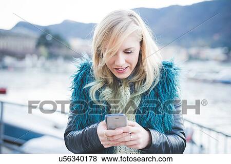 Stock Photo - "Young woman reading smartphone texts at Lake Como, Como, Italy". Fotosearch