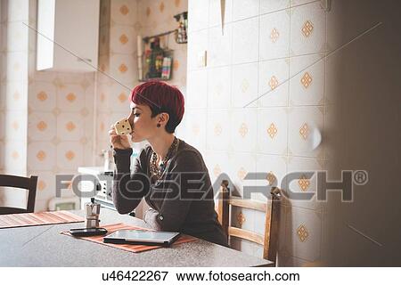 Young woman sitting at table drinking coffee View Large Photo Image Stock Photo - Young woman sitting at table drinking coffee. Fotosearch