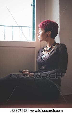 "Young woman sitting by window, holding smartphone" View Large Photo Image Stock Image - "Young woman sitting by window, holding smartphone". Fotosearch