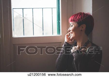 Stock Photograph - "Young woman sitting by window, talking on mobile phone". Fotosearch