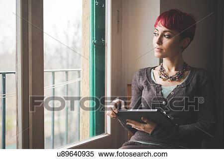 Stock Photography - "Young woman sitting by window, using digital tablet". Fotosearch
