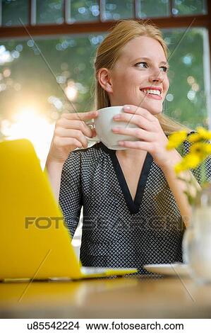 "Young woman sitting in cafe, drinking coffee, using laptop" View Large Photo Image Picture - "Young woman sitting in cafe, drinking coffee, using laptop". Fotosearch