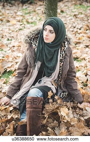 Young woman sitting in park amongst autumn leaves View Large Photo Image Stock Image - Young woman sitting in park amongst autumn leaves. Fotosearch