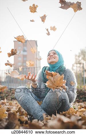 Young woman sitting in park throwing autumn leaves View Large Photo Image Stock Image - Young woman sitting in park throwing autumn leaves. Fotosearch