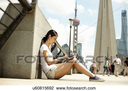 "Young woman sitting on bridge looking at digital tablet, The Bund, Shanghai, China" View Large Photo Image Stock Image - "Young woman sitting on bridge looking at digital tablet, The Bund, Shanghai, China". Fotosearch