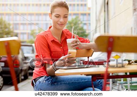 "Young woman sitting outside cafe with drink, using mobile phone" View Large Photo Image Stock Photo - "Young woman sitting outside cafe with drink, using mobile phone". Fotosearch