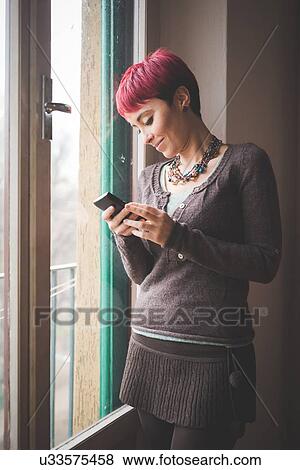 "Young woman standing by window, using smartphone" View Large Photo Image Stock Photo - "Young woman standing by window, using smartphone". Fotosearch