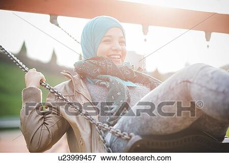 Stock Photo - Young woman swinging on playground swing. Fotosearch