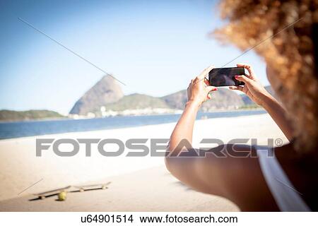 "Young woman taking photograph of view, using smartphone, rear view" View Large Photo Image Picture - "Young woman taking photograph of view, using smartphone, rear view". Fotosearch