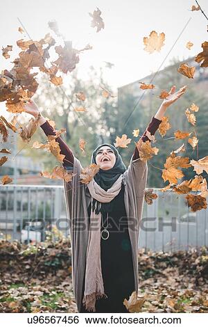Stock Photograph - Young woman throwing autumn leaves in park. Fotosearch