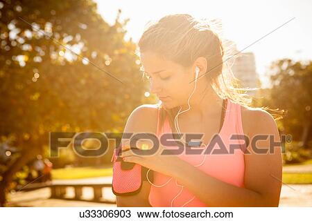 Young woman training and selecting music for earphones in park View Large Photo Image Stock Image - Young woman training and selecting music for earphones in park. Fotosearch