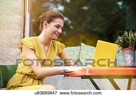 Young woman using laptop outside cafe View Large Photo Image Stock Photo - Young woman using laptop outside cafe. Fotosearch
