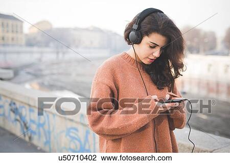 Stock Image - Young woman wearing headphones choosing music on smartphone. Fotosearch