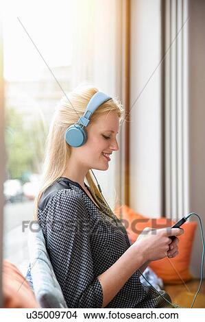 "Young woman, wearing headphones, sitting in cafe, holding smartphone" View Large Photo Image Picture - "Young woman, wearing headphones, sitting in cafe, holding smartphone". Fotosearch