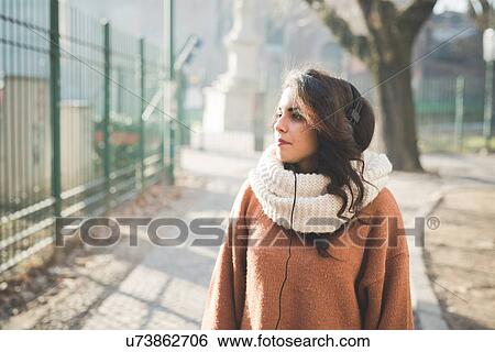 Stock Photograph - Young woman wearing headphones strolling in park. Fotosearch