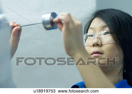 Stock Image - Young woman wearing safety glasses with metal component. Fotosearch