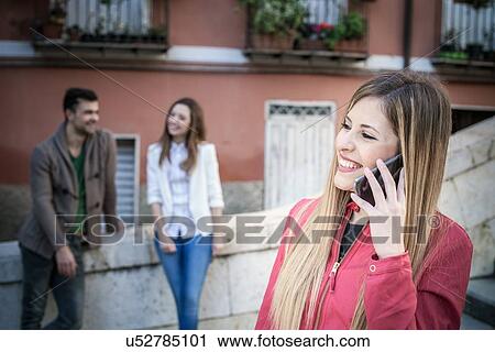 Stock Image - "Young woman with friends talking on smartphone, Cagliari, Sardinia, Italy". Fotosearch