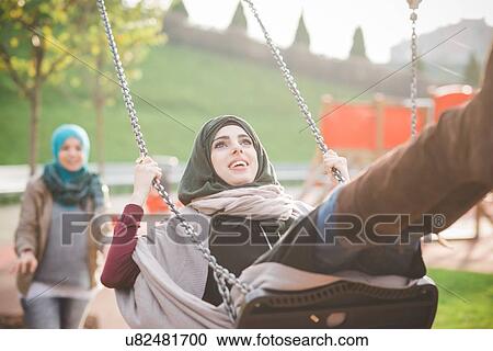 Stock Image - Young women swinging on playground swing. Fotosearch