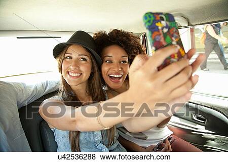 Stock Photo - Young women taking photo of themselves in car. Fotosearch