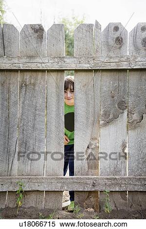 Boy (6-7) looking through hole in fence View Large Photo Image Stock Photography - Boy (6-7) looking through hole in fence. Fotosearch