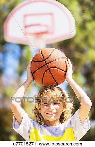 Stock Image - Boy (8-9) caring basketball on head. Fotosearch