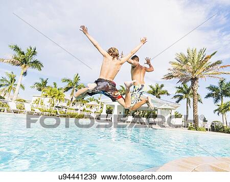 Boy (8-9) diving into swimming pool with his brother View Large Photo Image Stock Photo - Boy (8-9) diving into swimming pool with his brother. Fotosearch