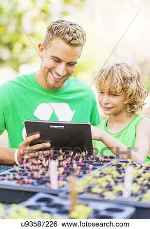 Stock Photograph - Boy (8-9) using tablet pc with his brother in garden. Fotosearch