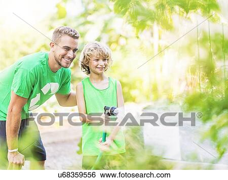 Stock Photograph - Boy (8-9) watering plants with his brother. Fotosearch