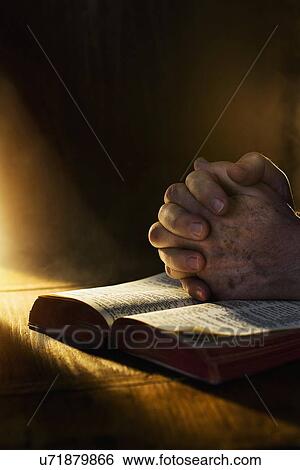 Stock Photograph - Close up of hands clasped on open Bible. Fotosearch