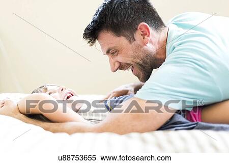 Stock Photography - Father playing with daughter (4-5) on bed. Fotosearch